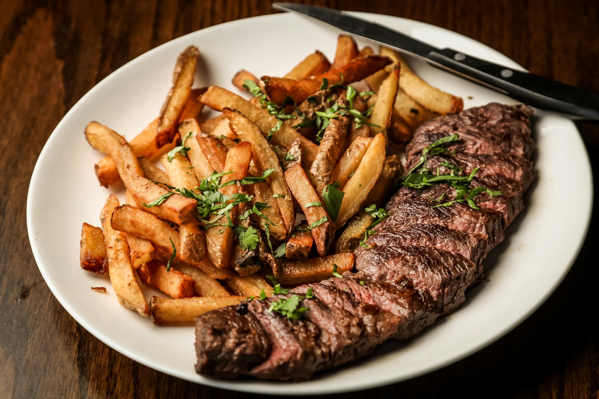 Gedeckter Teller mit herzhaftem Braten und knusprigen Pommes auf rustikalem Holztisch — gutbürgerliche Küche im Gasthaus